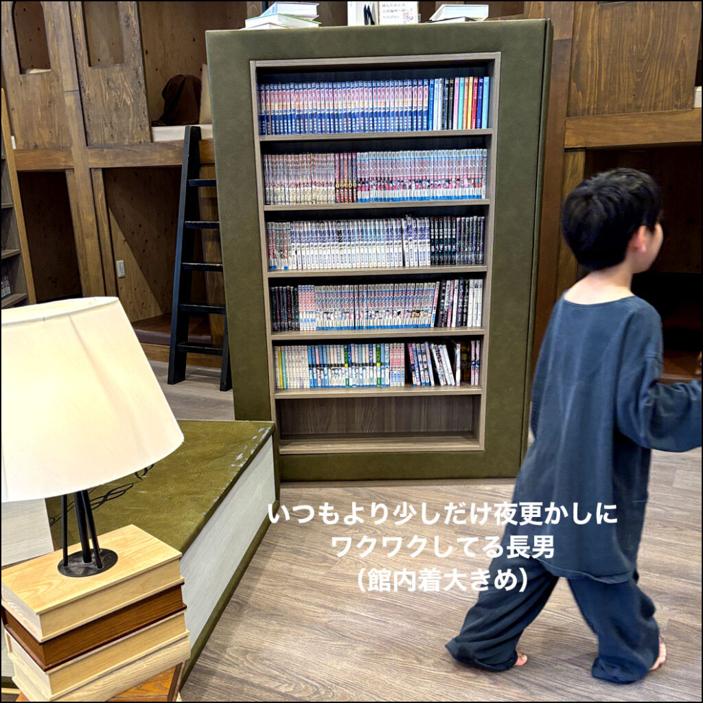 本棚の前を歩く長男。大きめの館内着を着て、いつもより少しだけ夜更かしできることにワクワクしている後ろ姿